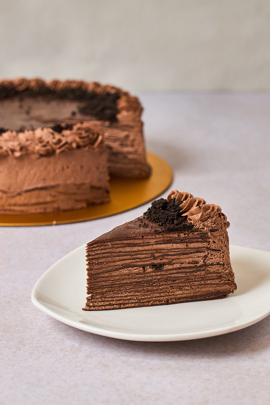 single slice cut out from a round chocolate crepe cake, revealing multiple delicate layers, displayed on a white plate